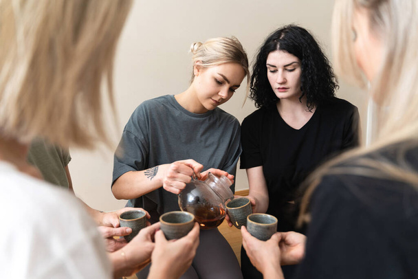 Young woman is pouring hot tea to her friends sitting around during a tea ceremony. - Φωτογραφία, εικόνα