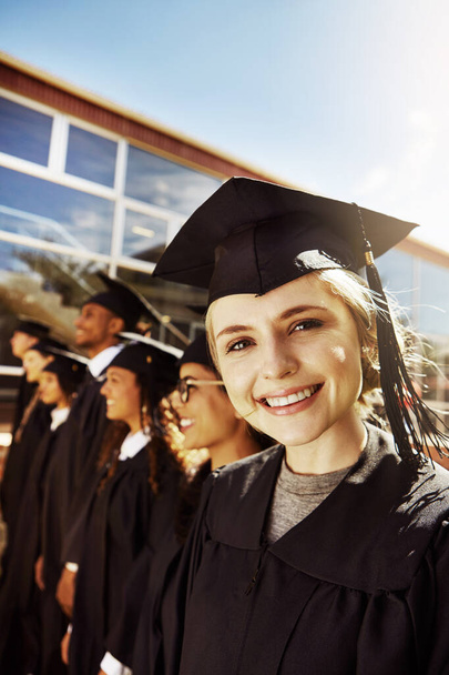 Elle se dirigea vers un brillant avenir. Portrait d'un étudiant souriant le jour de la remise des diplômes avec ses camarades de classe en arrière-plan - Photo, image