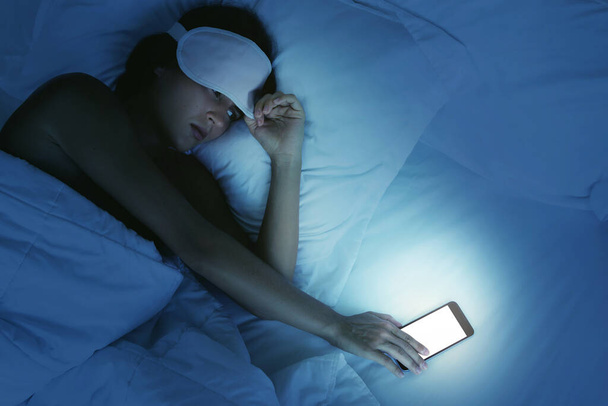 Sleepy woman lying in the bed and looking on smartphone at night - Fotografie, Obrázek