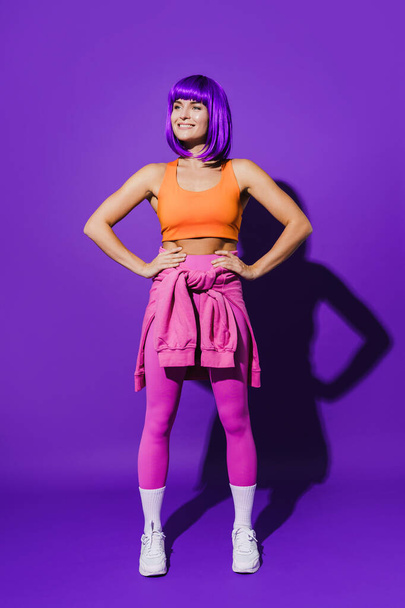 Portrait of cheerful woman wearing colorful sportswear sitting against purple background - Fotografie, Obrázek