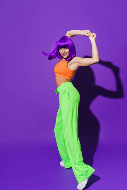 Carefree active woman dancer wearing colorful sportswear performing against purple background - Photo, Image