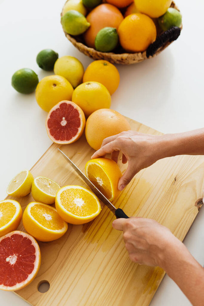 Closeup of female hands with knife slicing citrus fruits on cutting board for homemade fresh juice - Foto, Bild
