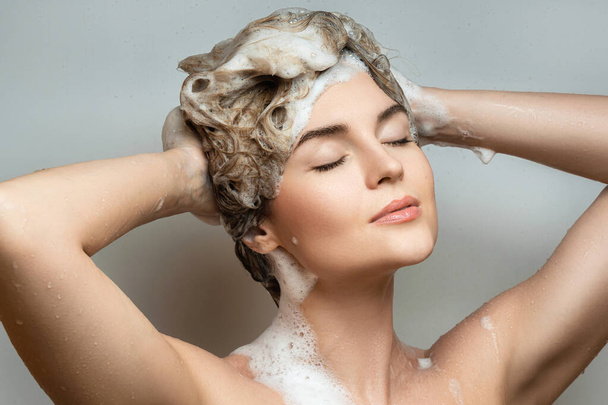 Portrait of young beautiful woman is washing her hair with a shampoo - Foto, immagini