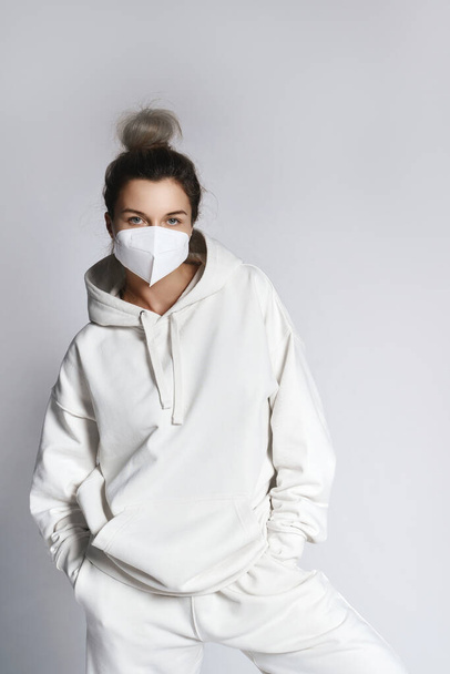 Young woman wearing white hoodie and ffp2 respirator mask against gray background - Фото, зображення
