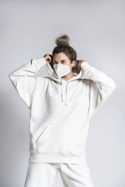 Young woman wearing white hoodie and ffp2 respirator mask against gray background - Foto, Imagem