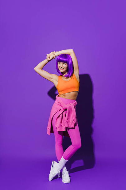 Portrait of cheerful woman wearing colorful sportswear sitting against purple background - Photo, Image