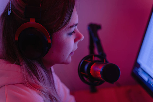 Young woman blogger using condenser microphone during online podcast in room with neon light - Foto, afbeelding
