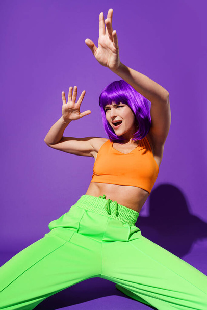Carefree active woman dancer wearing colorful sportswear performing against purple background - Fotoğraf, Görsel