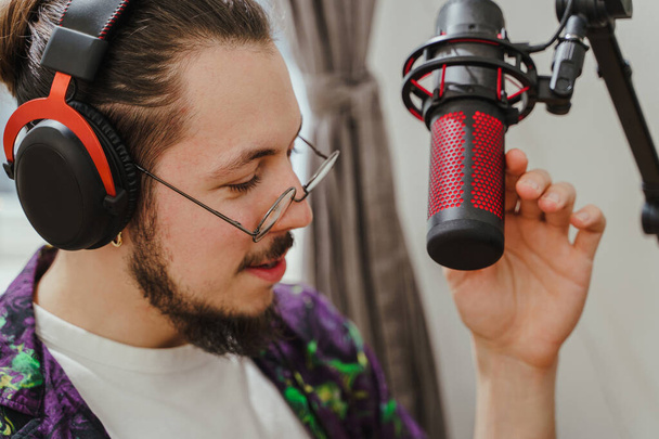 Young  stylish man blogger using headphones and condenser microphone  during online podcast stream  - Photo, Image