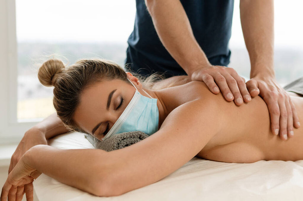 Young woman wearing prevention mask during back massage session - Foto, Imagem
