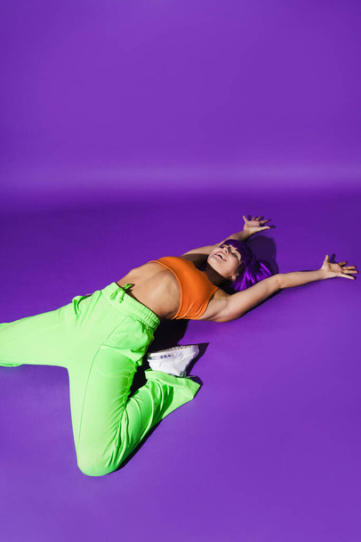 Carefree active woman dancer wearing colorful sportswear performing against purple background - Фото, изображение