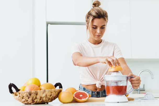 Young woman with a lot of citrus fruits during fresh grapefruit juice preparation at home - Fotoğraf, Görsel