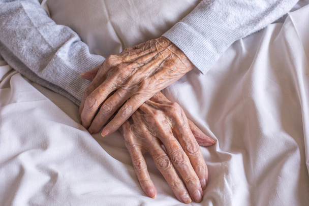 Egy idős nő kezei összezáródnak egy ágyon egy kórházban. Öregedési folyamat, idős nők. Kiváló minőségű fénykép - Fotó, kép