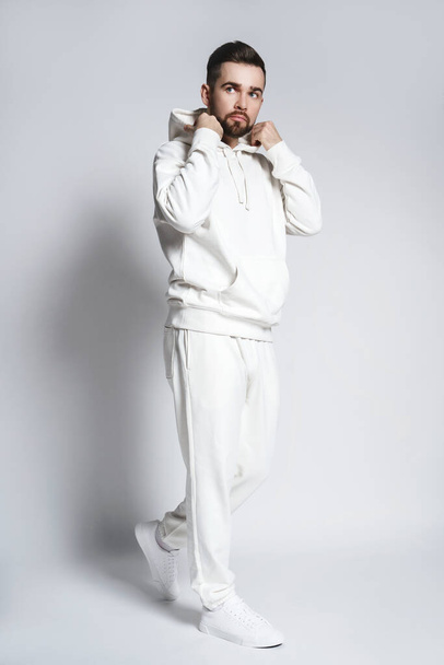 Handsome man wearing blank white hoodie and pants posing on gray background - Foto, afbeelding