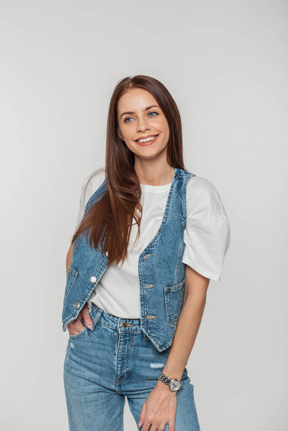 Menina elegante bonita alegre com um sorriso na moda roupas jeans em um fundo branco no estúdio - Foto, Imagem