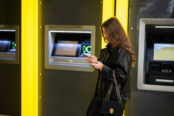 Young brunette girl withdrawing money from credit card at yellow ATM. - Foto, Imagem