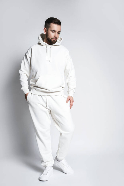 Handsome man wearing blank white hoodie and pants posing on gray background - Фото, зображення