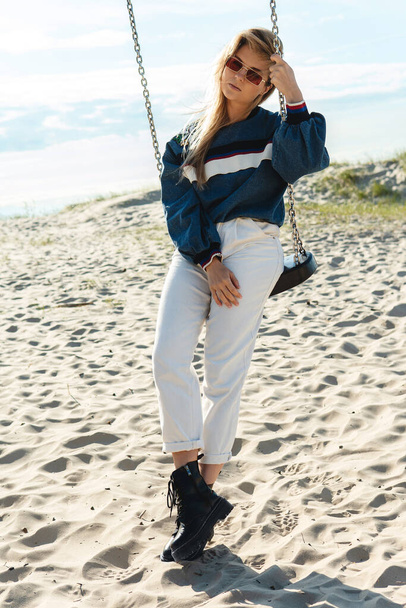 Young pretty woman is sitting on the swing and relaxing at the sandy beach. - Foto, afbeelding