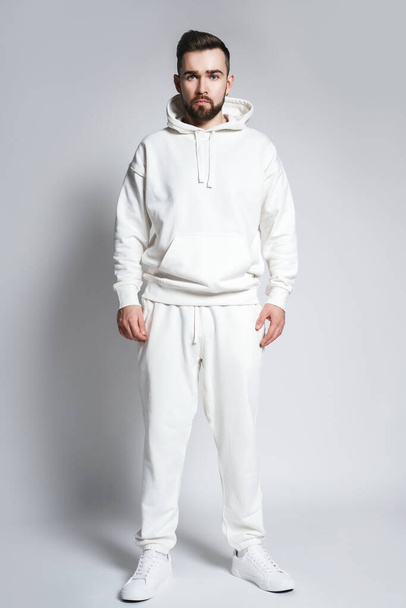 Handsome man wearing blank white hoodie and pants posing on gray background - Foto, Imagen
