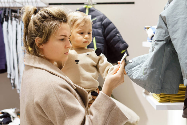 Young woman with her baby son choosing clothing in clothes store - Fotografie, Obrázek