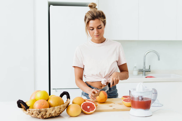 Young woman with a lot of citrus fruits during fresh grapefruit juice preparation at home - Foto, Bild