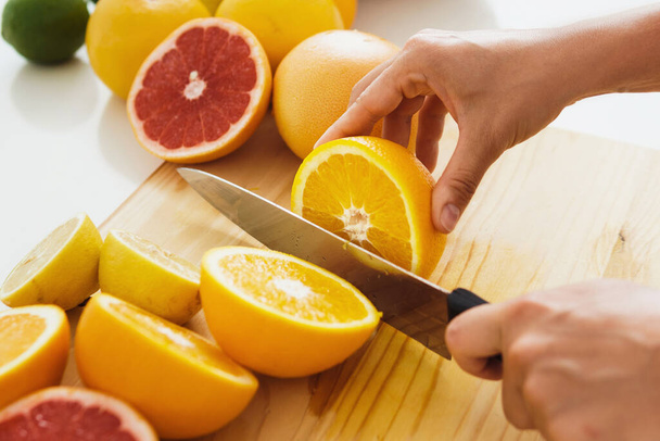 Closeup of female hands with knife slicing citrus fruits on cutting board for homemade fresh juice - Фото, изображение