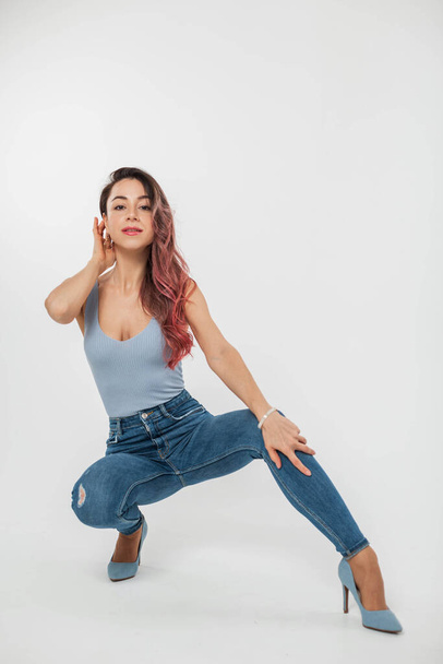 Beautiful young stylish woman in denim clothes with a top, jeans and heels sits and poses on a white background - 写真・画像
