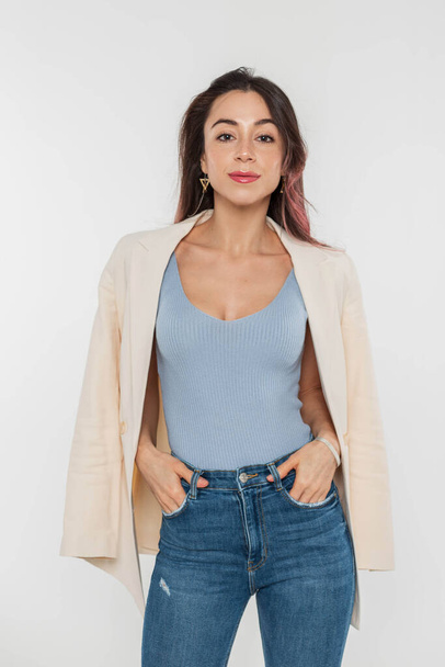 Pretty fashionable young woman with pink hair in blue trendy top and jeans with blazer on a white background - Фото, изображение