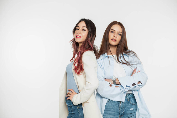Two stylish beautiful young female models girlfriends in fashion clothes with jeans, a shirt and a blazer posing on a white background - Photo, Image