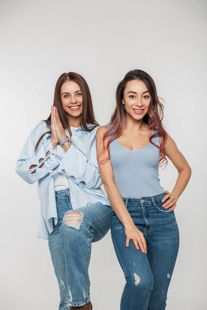 Dwa szczęśliwe piękne dziewczyny przyjaciół w modzie casual ubrania dżinsy z jeansów pozowanie na białym tle - Zdjęcie, obraz