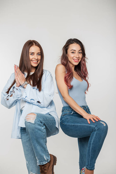 Twee mooie jonge modieuze meisje vrienden in stijlvolle denim kleding poseren en plezier hebben op een witte achtergrond - Foto, afbeelding