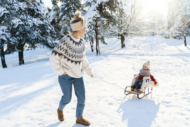 Mother and her cute little son wearing warm sweaters are having on a sledding hill during sunny winter day - Fotoğraf, Görsel