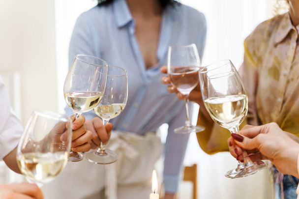 Close-up shot of young women friends clinking glasses filled with white wine - 写真・画像