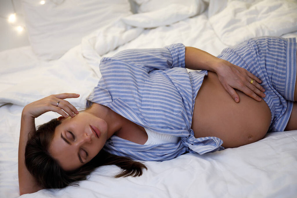 Молода красива і чуттєва вагітна жінка лежить на ліжку в її затишній квартирі
 - Фото, зображення