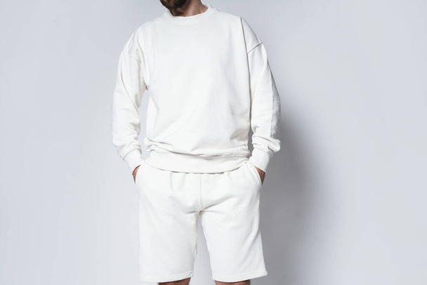 Man wearing white blank sweatshirt and shorts against gray background - Zdjęcie, obraz
