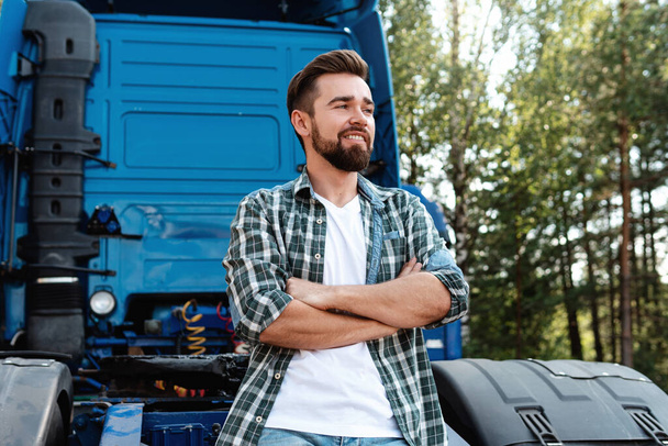 Young smiling male truck driver beside his blue cargo truck is happy about his work - Foto, Bild