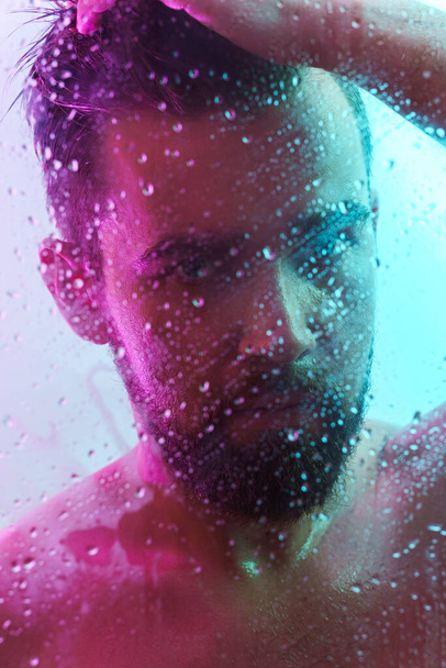 Portrait of handsome young man captured through wet glass in colorful neon light - Fotoğraf, Görsel