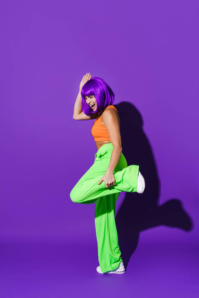 Carefree active woman dancer wearing colorful sportswear having fun against purple background - 写真・画像