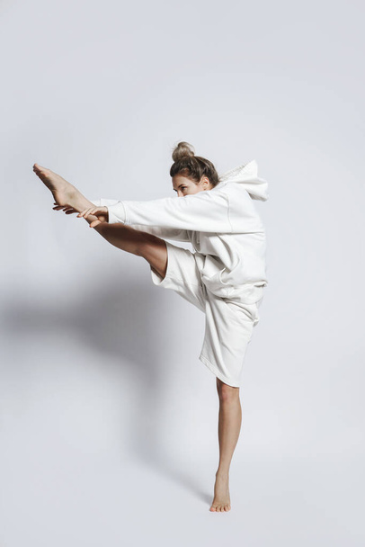 Young woman dancer wearing white clothes is performing against gray background - Foto, Imagem