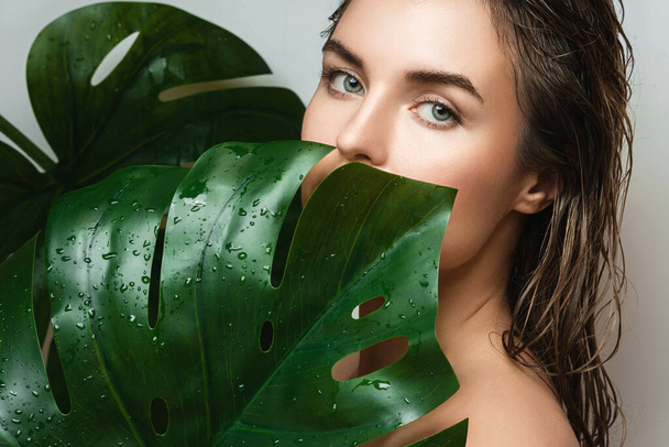 Portrait of beautiful young woman with a smooth skin holding Monstera deliciosa plant leaf - Φωτογραφία, εικόνα