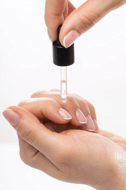 Female hands and bottle of nourishing cuticle oil with a dropper on white background  - Zdjęcie, obraz