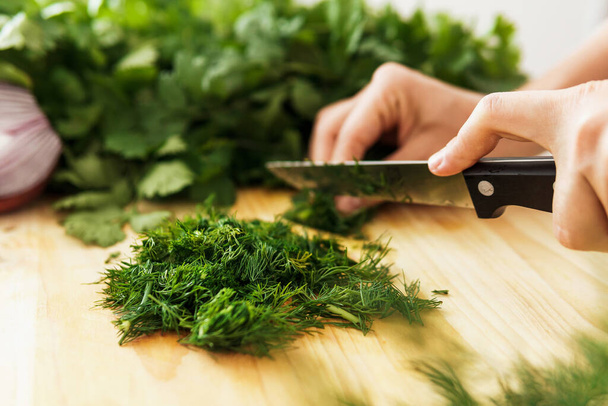Closeup of female hands with knife chopping dill on wooden cutting board - Foto, immagini