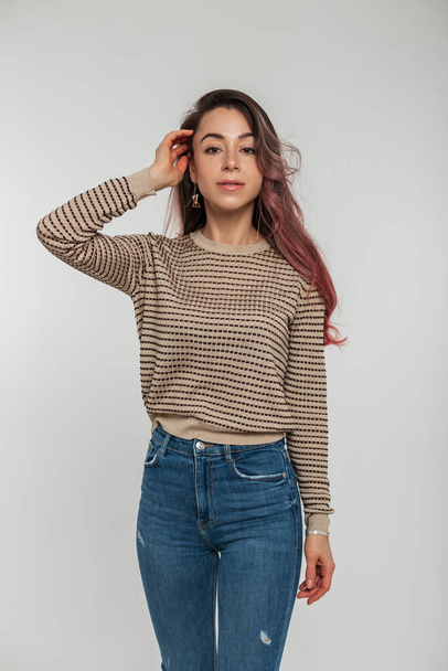 Fashionable beautiful stylish woman with pink hair in a stylish pullover and blue jeans posing on a white background - Photo, Image