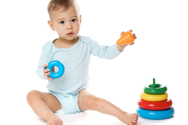 Adorable little boy in a romper is sitting and playing with plastic toy on white background. - Foto, Imagen