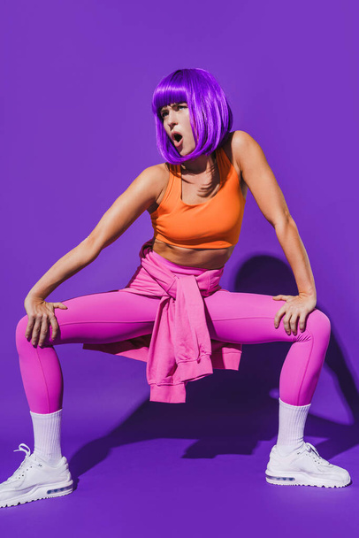 Carefree young woman dancer wearing colorful sportswear performing against purple background - Фото, зображення