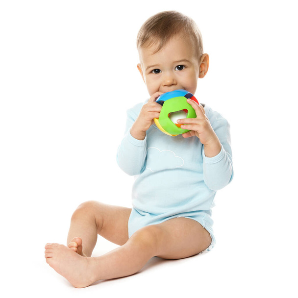 Adorable little boy in a romper is sitting and playing with plastic toy, putting it in his mouth on white background. - Foto, Imagen
