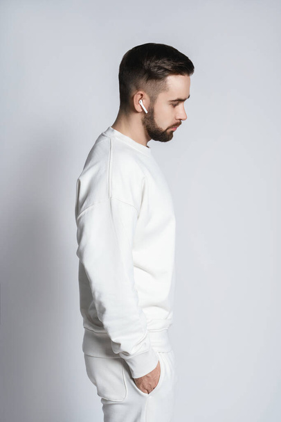 Handsome man wearing white sweatshirt with wireless earbuds against gray background - Φωτογραφία, εικόνα
