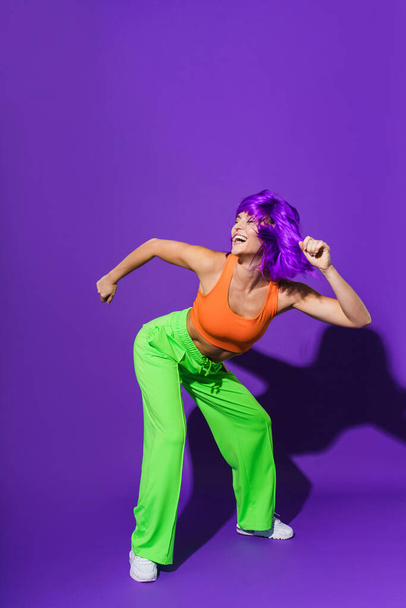 Carefree active woman dancer wearing colorful sportswear having fun against purple background - 写真・画像