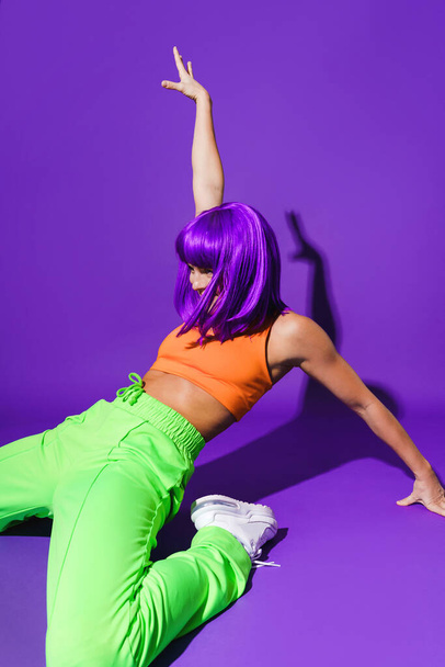 Carefree active woman dancer wearing colorful sportswear performing against purple background - Zdjęcie, obraz