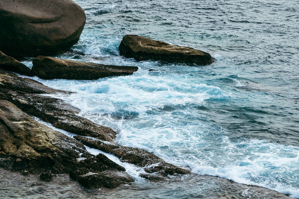 Closeup shot of foamy waves crashing on a rocky coast during a high tide. - Фото, изображение